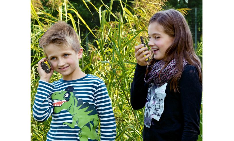 two young children using walkie talkies in a field