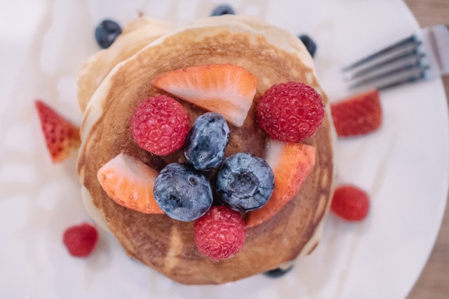 a stack of pancakes with blueberries, raspberries, and strawberries