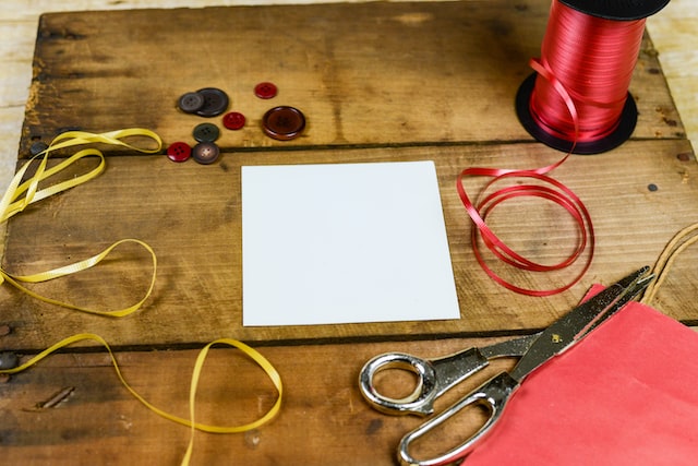 Square of white paper and scissors on wooden table