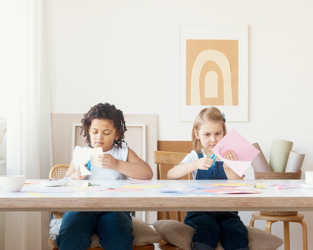 Two girls sat at a table cutting paper with scissors