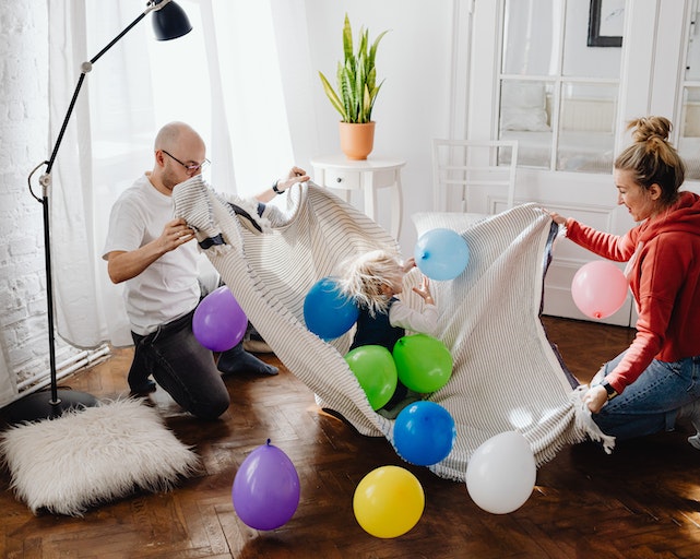 Smiling mum, dad, and daughter playing indoor games with balloons