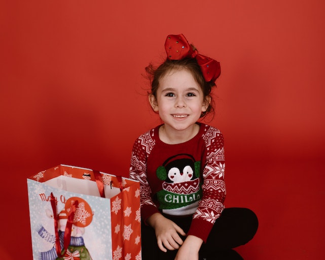 Young girl wearing a red Christmas jumper with red background